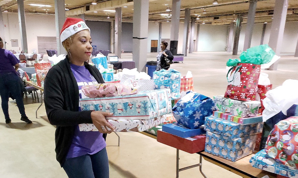 Volunteer carrying Christmas gift to table with several angel tree gifts.