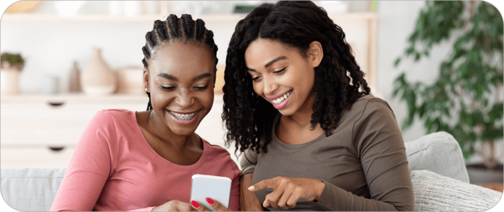 Two young Gen Z girls smiling while looking at a mobile phone