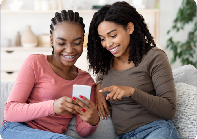 Two young Gen Z girls smiling while looking at a mobile phone